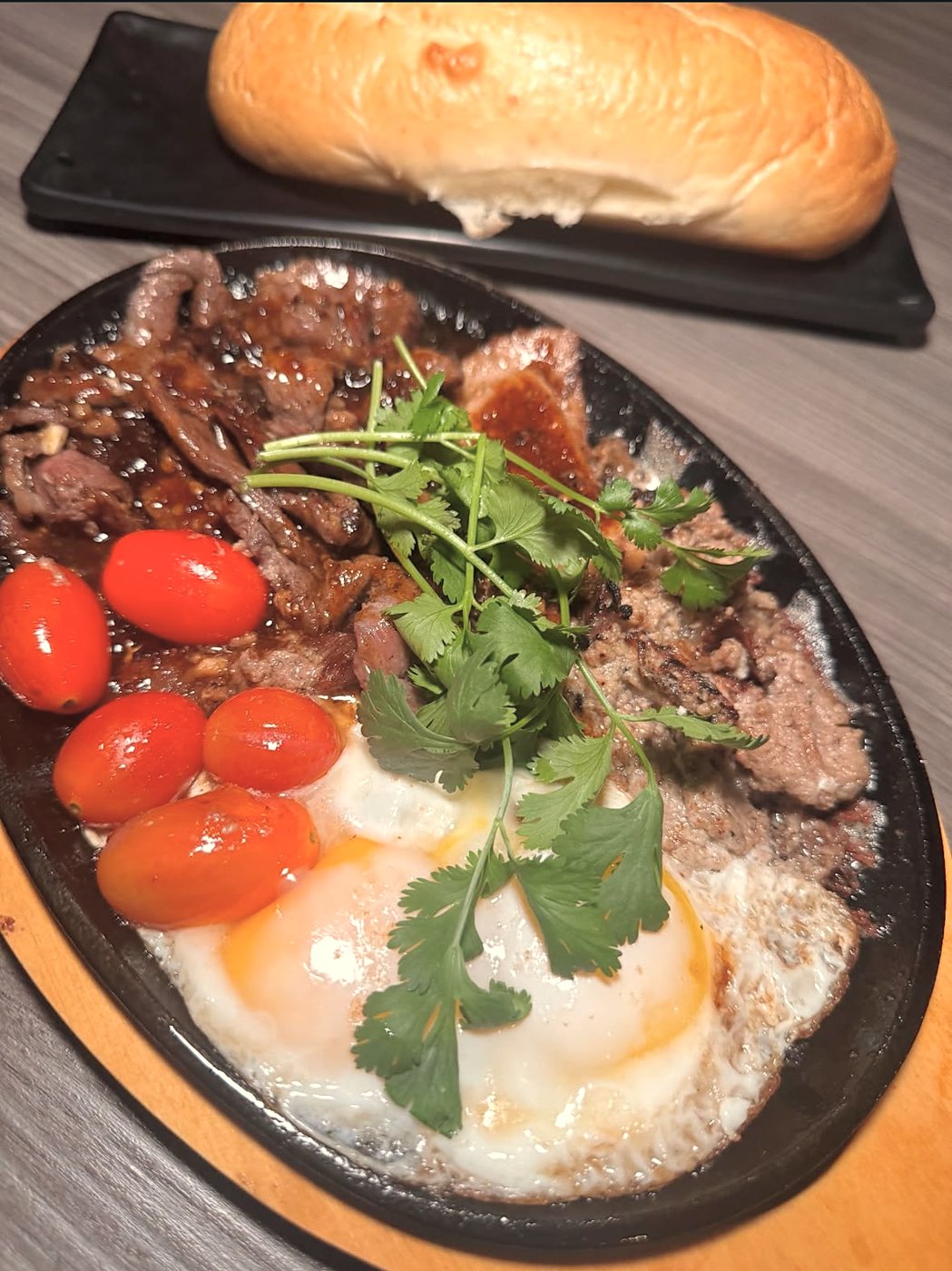 Bò Né: sizzling steak with eggs, cherry tomatoes and cilantro, baguette on the side